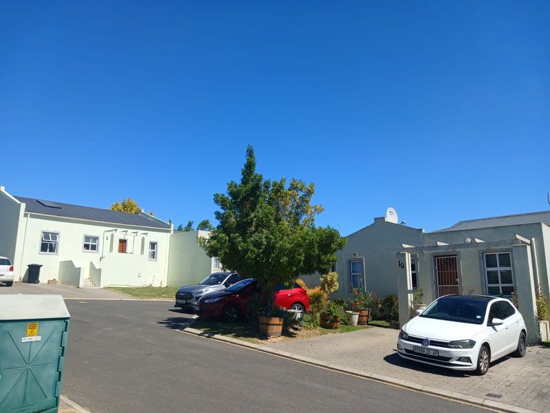 A street-level view of a residential complex featuring paved driveways, light-colored exterior walls, and metal roofing under a clear blue sky.