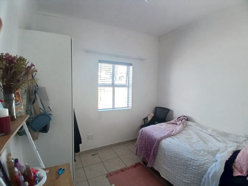 A functional bedroom featuring tiled flooring, a built-in wardrobe, and a window fitted with venetian blinds.