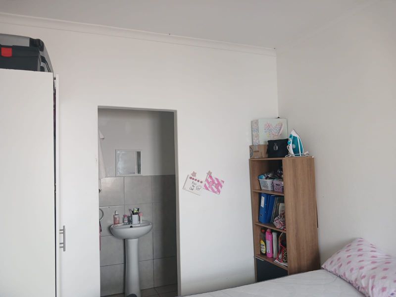 A bedroom featuring a built-in wardrobe and an en-suite area with a pedestal basin and tiled splashback.