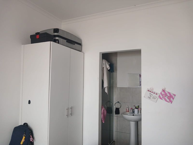 A bedroom featuring a built-in wardrobe and an en-suite bathroom with a pedestal basin and shower enclosure.