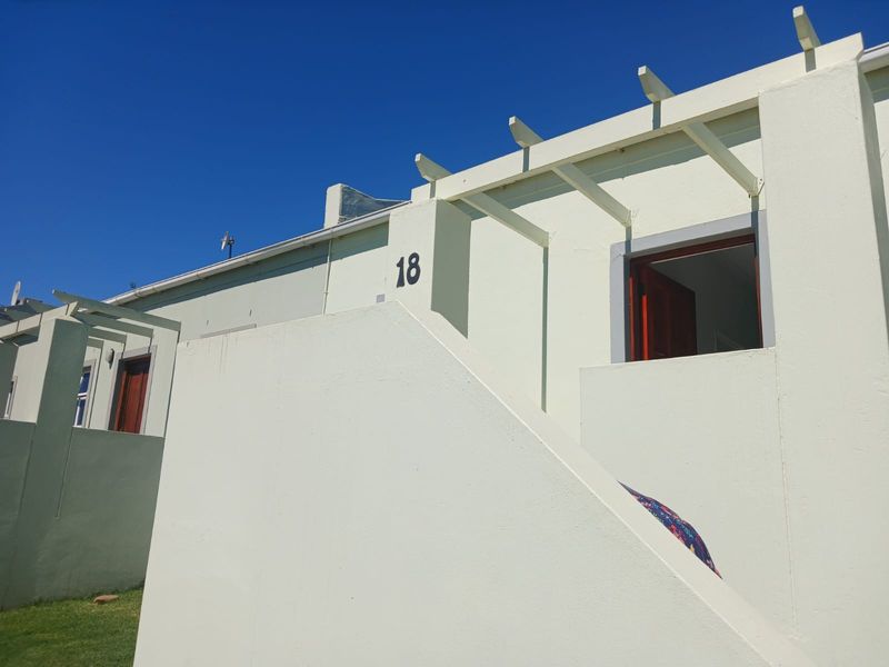 A clear view of the front facade of unit 18, featuring a painted masonry exterior, a structural pergola, and an external staircase.