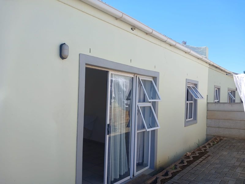 Rear exterior view of the house featuring a sliding glass door, top-hung windows, and a paved walkway along the side of the building.