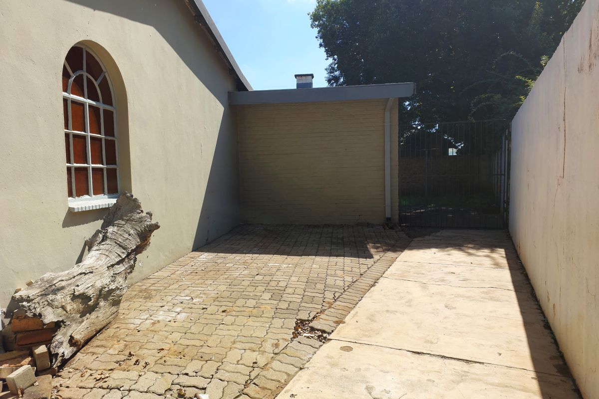 A rear exterior area featuring paved surfaces, a metal gate, and an arched window on the side of the building structure.