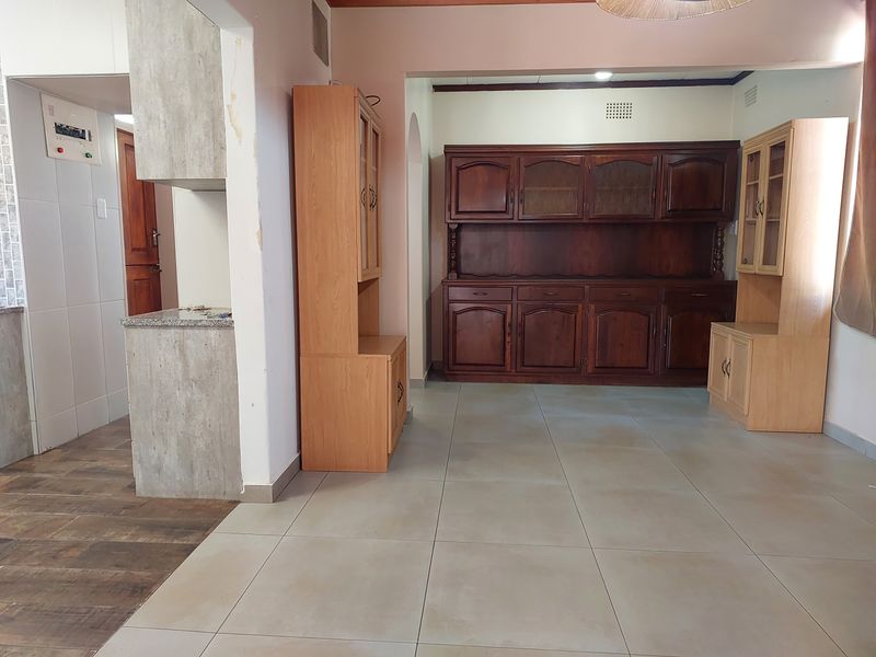 Open plan living and dining area featuring large format floor tiles, built-in wooden cabinetry, and a stone-topped breakfast counter.