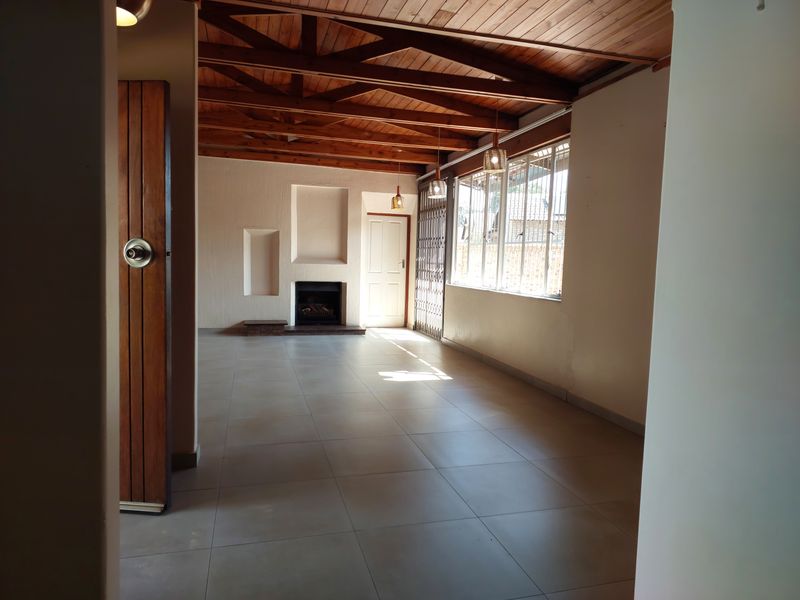 Spacious living area featuring exposed timber ceiling beams, tiled flooring, a built-in fireplace, and recessed wall niches, offering a bright and open atmosphere.