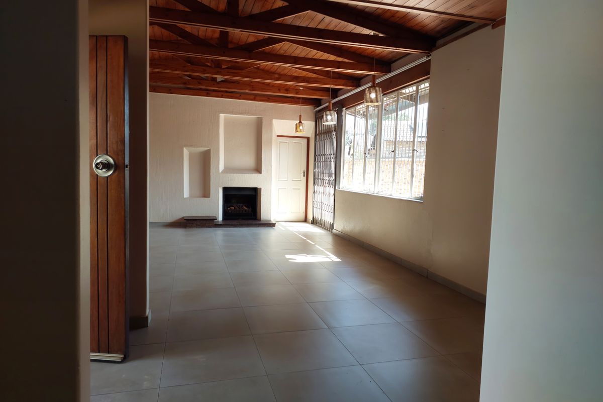 Spacious living area featuring exposed timber ceiling beams, tiled flooring, a built-in fireplace, and recessed wall niches, offering a bright and open atmosphere.