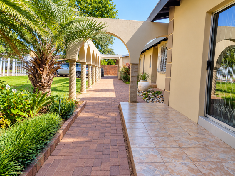 A well-maintained exterior patio area featuring a tiled floor, a brick-paved walkway, and a decorative arched colonnade leading along the side of the house.