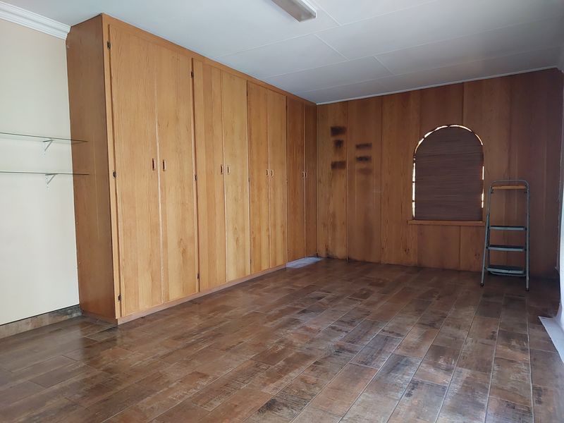 An empty bedroom featuring extensive built-in wooden cabinetry, tiled flooring, and a unique arched window. The space requires cosmetic updates to the wall finishes.