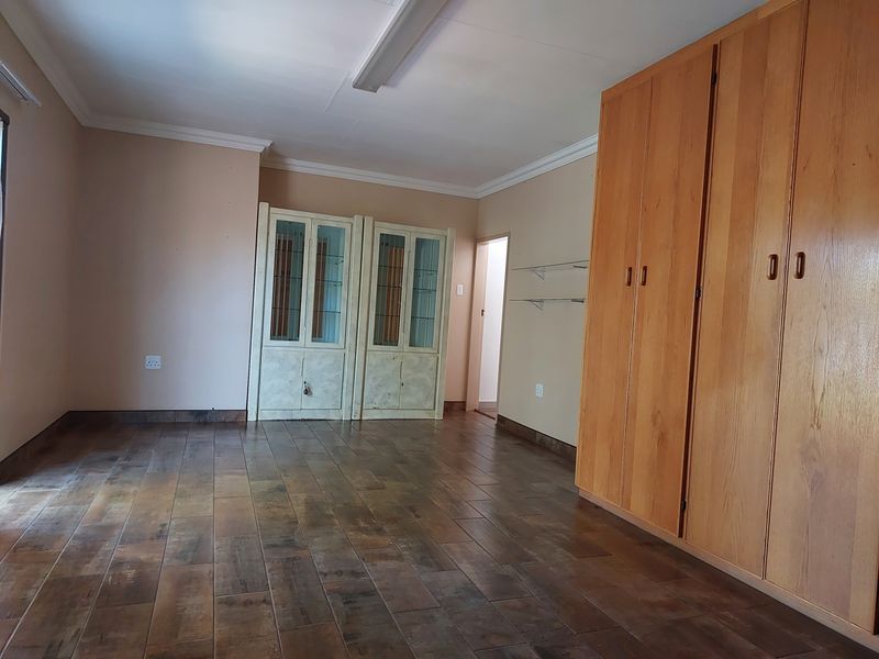 A spacious bedroom featuring wood-look tiled flooring, built-in cupboards, and additional built-in display cabinetry, offering a clean and functional living space.