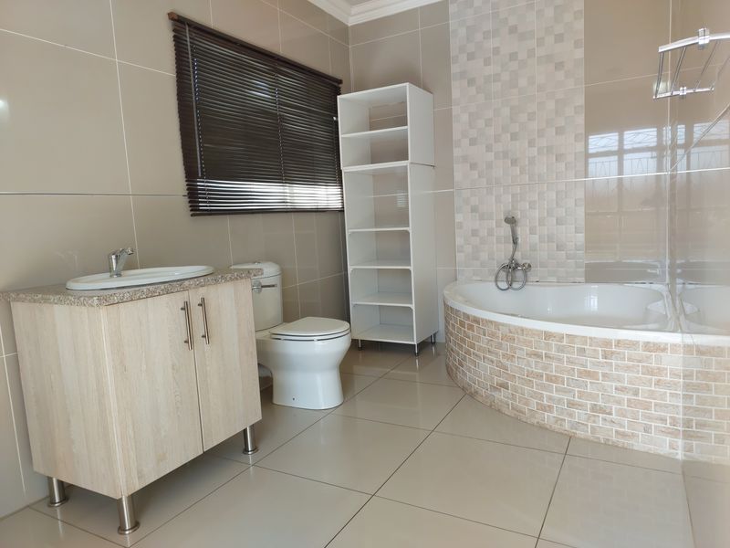 A well-maintained bathroom featuring a corner bathtub with decorative tiling, a vanity cabinet with a basin, and a toilet.