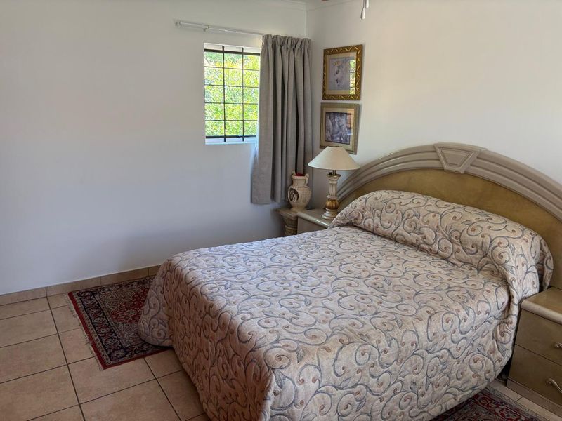 A functional bedroom featuring tiled flooring, a window with security bars, and a ceiling fan, offering a comfortable and secure living space.