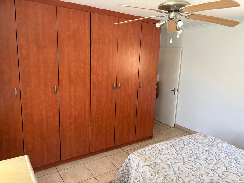 Bedroom featuring large wooden built-in cupboards, tiled flooring, and a ceiling fan, providing functional storage and climate control.