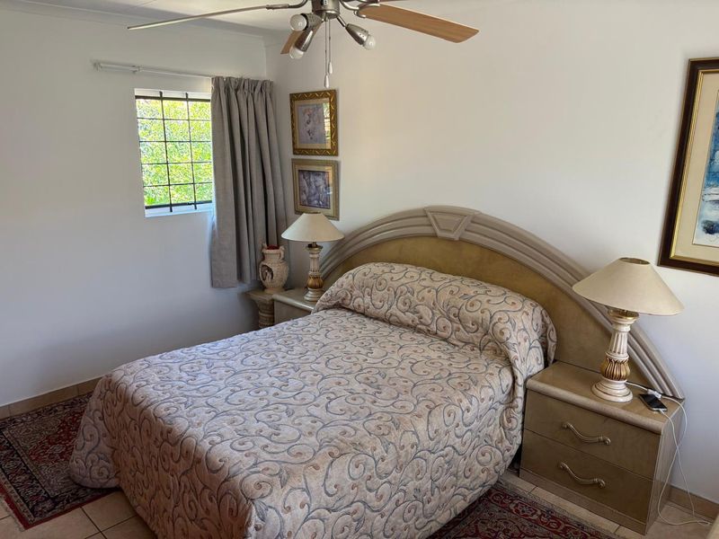 A bedroom featuring tiled flooring, a ceiling fan, and a window fitted with security bars.