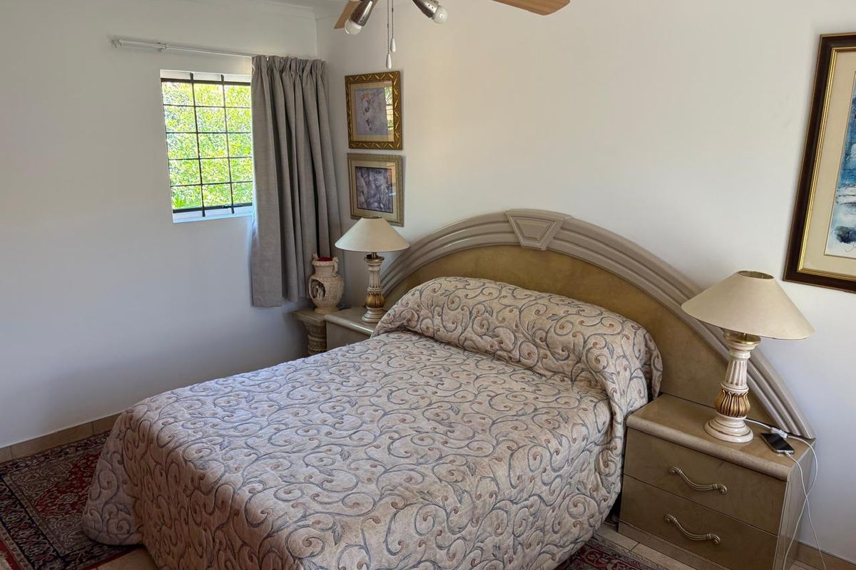 A bedroom featuring tiled flooring, a ceiling fan, and a window fitted with security bars.