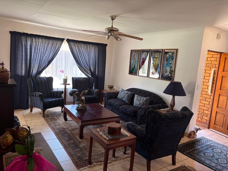 A comfortable living room featuring tiled flooring, a ceiling fan, and an exposed brick accent wall near the entrance.
