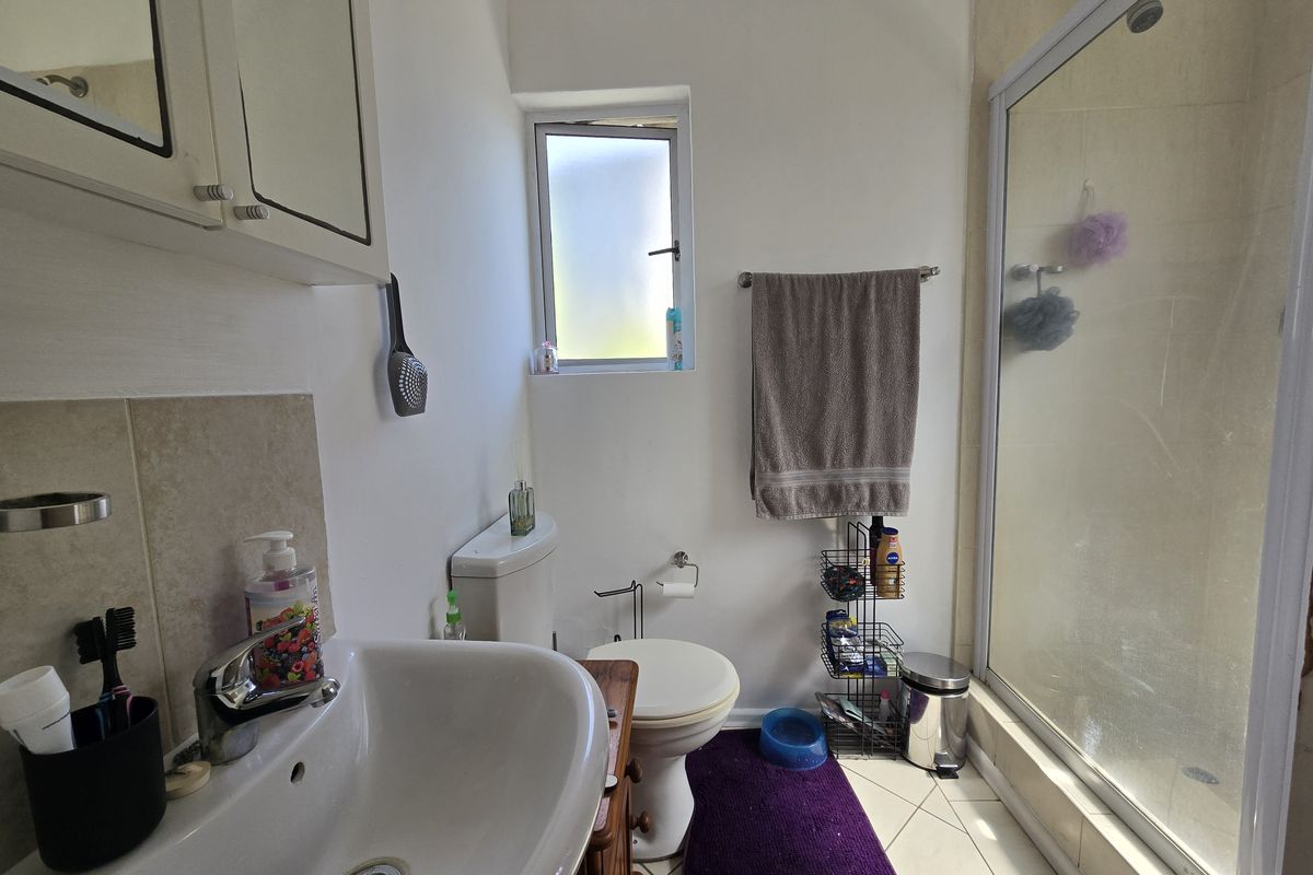 A functional bathroom featuring a pedestal basin, toilet, and a glass-enclosed shower with tiled surrounds and a medicine cabinet.