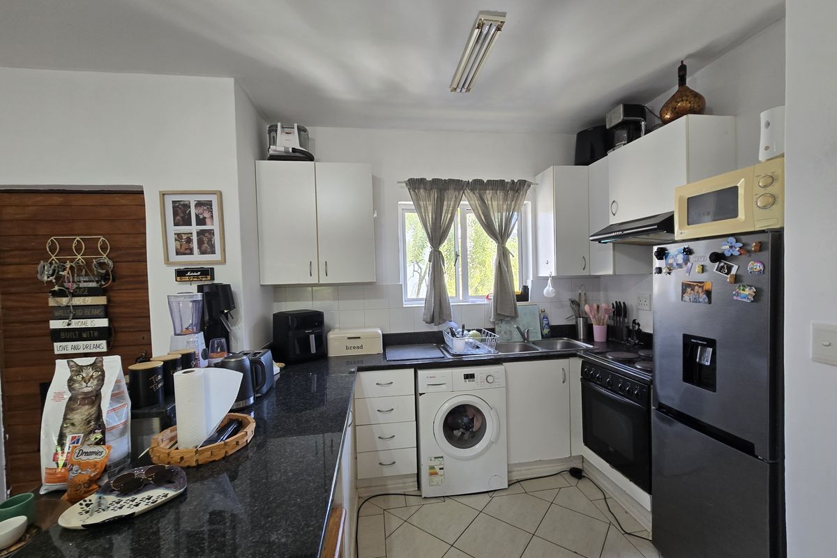 A functional kitchen featuring granite countertops, white cabinetry, integrated oven with extractor fan, and a built-in washing machine with tiled flooring.