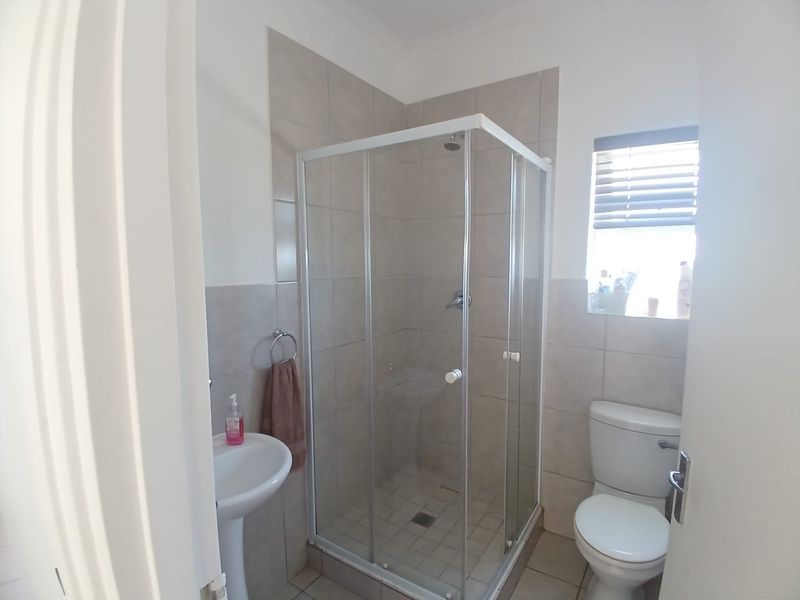 A functional bathroom featuring a corner shower enclosure, pedestal basin, and toilet with neutral wall and floor tiling.