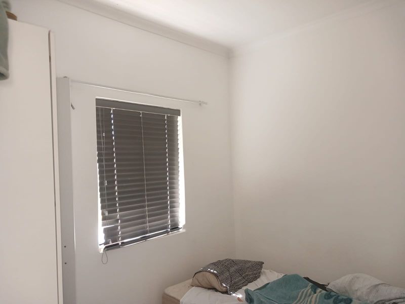 A simple bedroom featuring a window with venetian blinds and a built-in wardrobe.