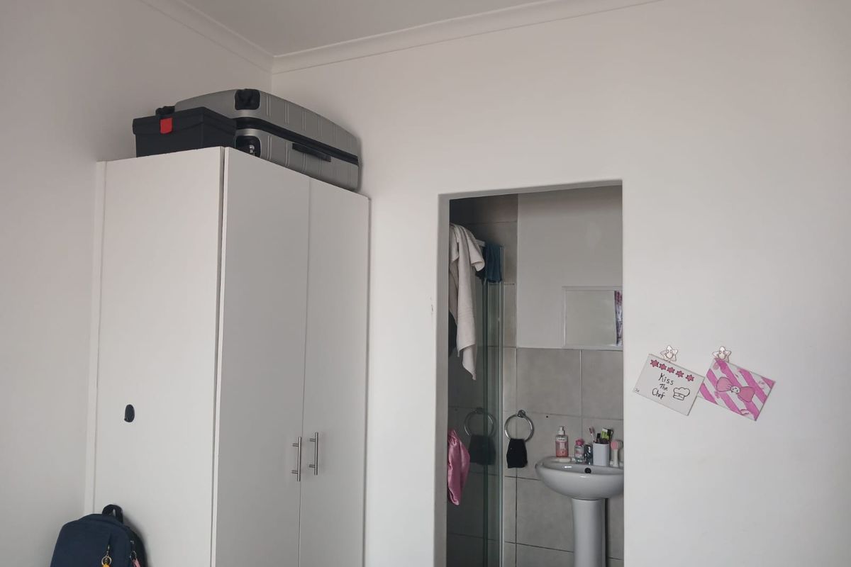 A bedroom featuring a built-in wardrobe and an en-suite bathroom with a pedestal basin and shower enclosure.