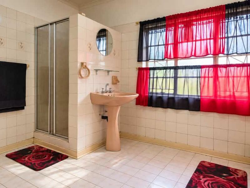 A dated bathroom featuring a pedestal basin, shower enclosure, and full-height ceramic wall tiling, offering potential for a modern renovation.