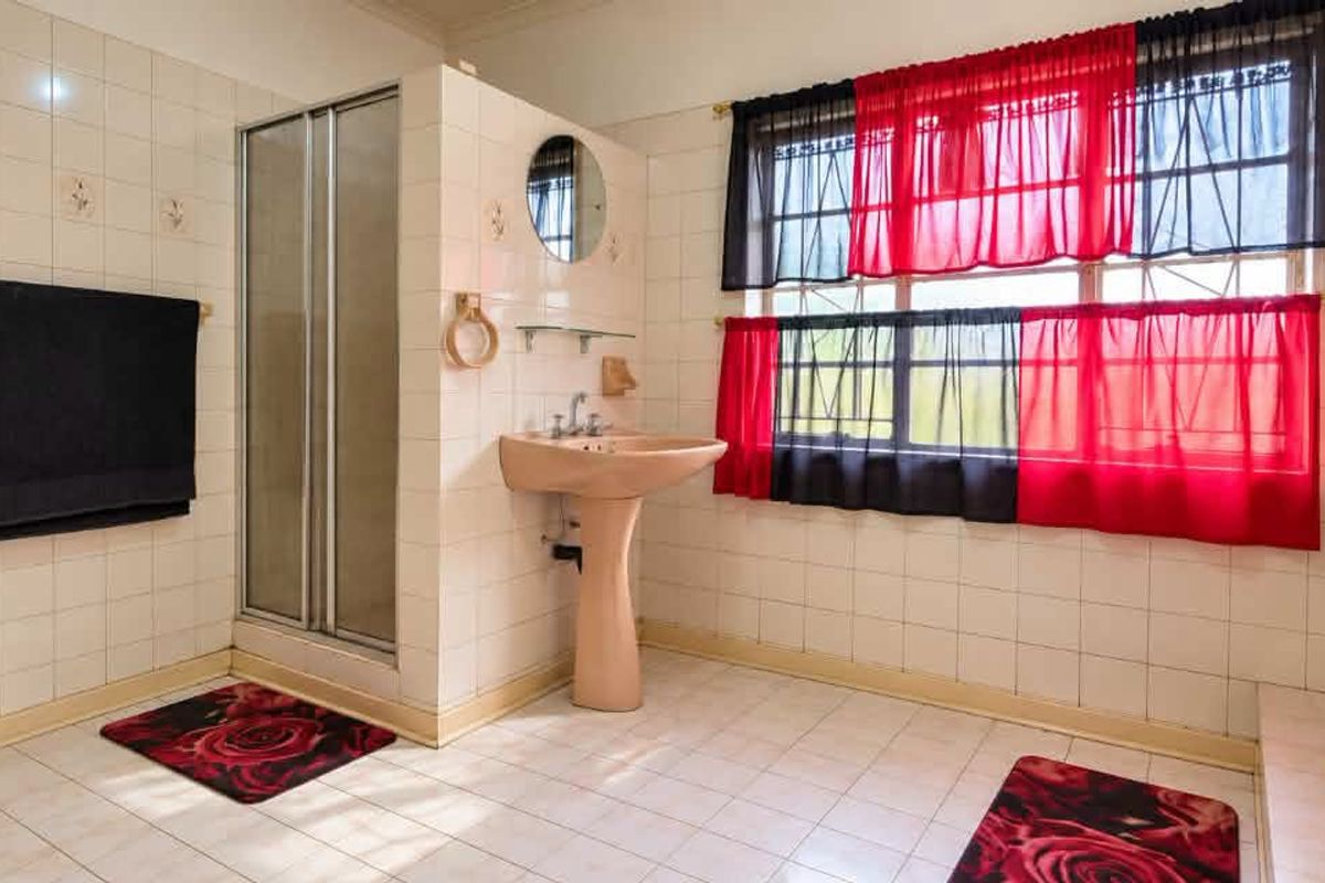 A dated bathroom featuring a pedestal basin, shower enclosure, and full-height ceramic wall tiling, offering potential for a modern renovation.