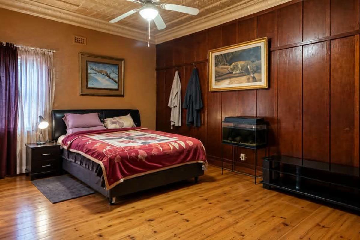 Spacious bedroom featuring classic timber wall paneling, a decorative pressed metal ceiling, a ceiling fan, and polished timber flooring.