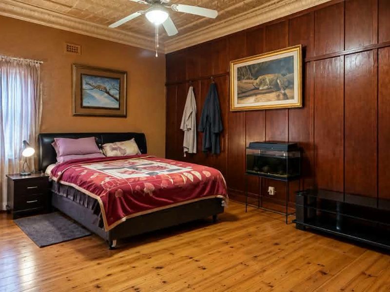 Spacious bedroom featuring classic timber wall paneling, a decorative pressed metal ceiling, a ceiling fan, and polished timber flooring.