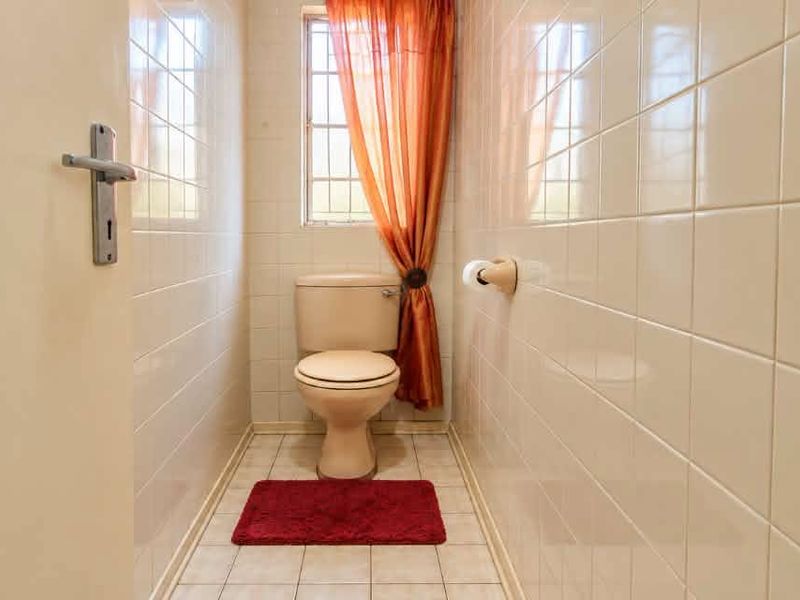 A compact guest bathroom featuring full-height ceramic wall tiling, tiled flooring, and a standard toilet suite.