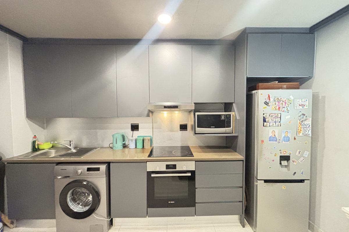 A modern kitchen featuring grey cabinetry, integrated oven, electric hob, extractor fan, built-in microwave, and tiled flooring.