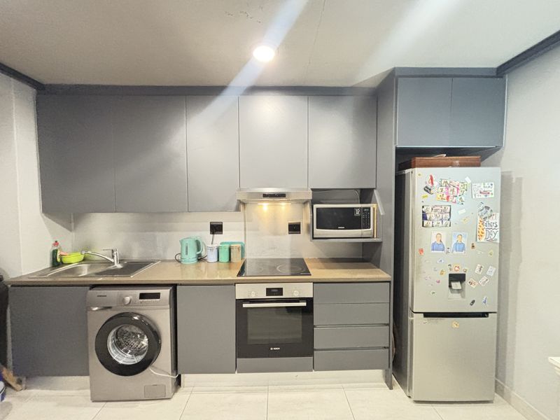 A modern kitchen featuring grey cabinetry, integrated oven, electric hob, extractor fan, built-in microwave, and tiled flooring.