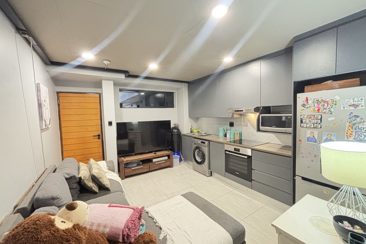 Modern open-plan living area featuring a sleek kitchen with integrated appliances, tiled flooring, and recessed lighting, creating a functional and contemporary space.