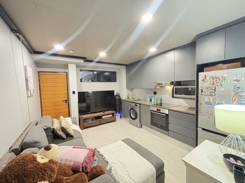 Modern open-plan living area featuring a sleek kitchen with integrated appliances, tiled flooring, and recessed lighting, creating a functional and contemporary space.