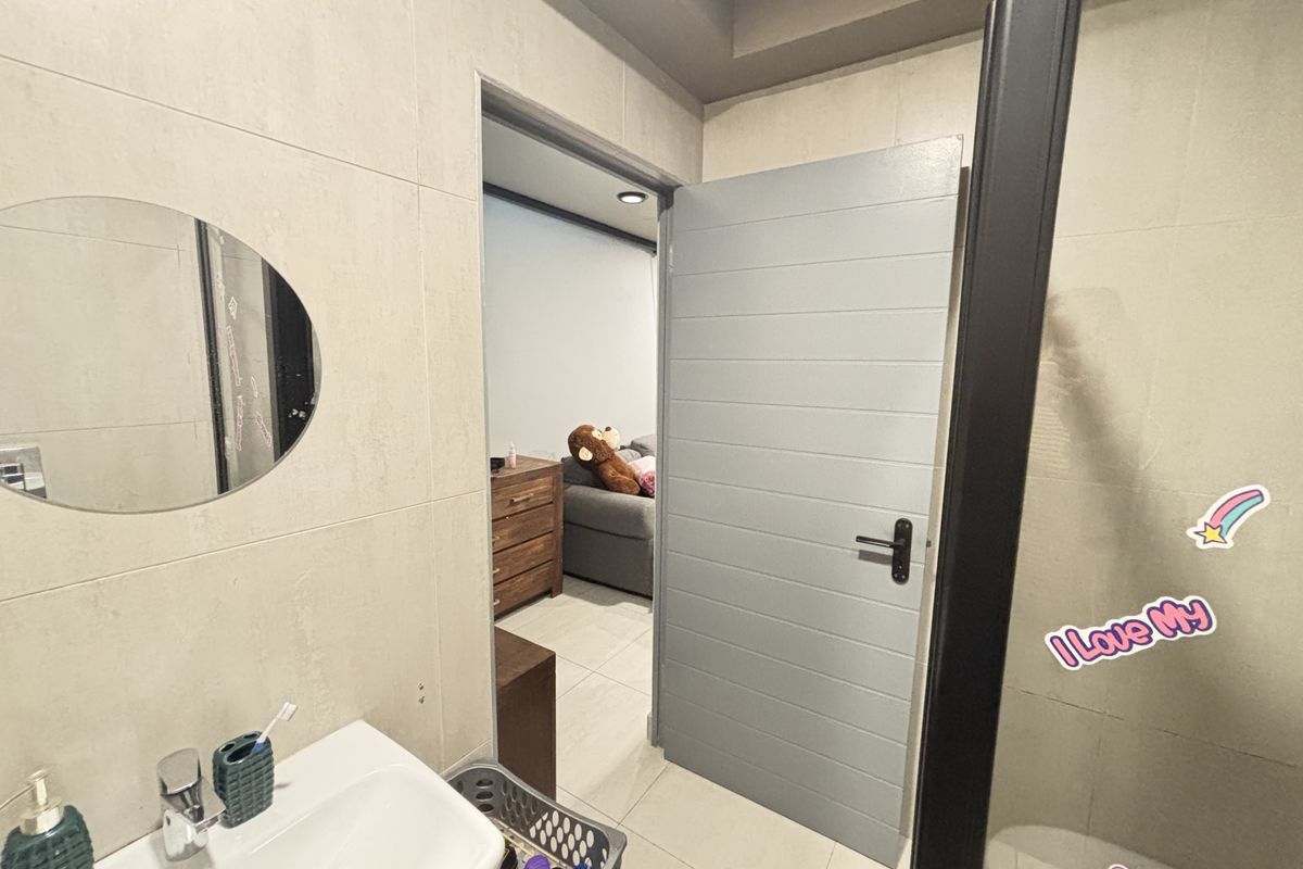 A modern bathroom featuring tiled walls and flooring, a wall-mounted basin with chrome fixtures, and a contemporary internal door leading to an adjacent room.