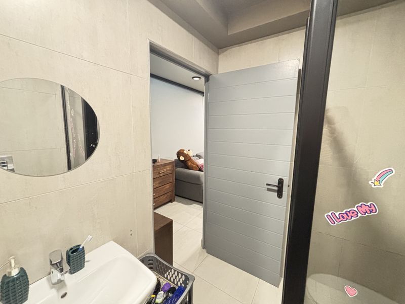 A modern bathroom featuring tiled walls and flooring, a wall-mounted basin with chrome fixtures, and a contemporary internal door leading to an adjacent room.