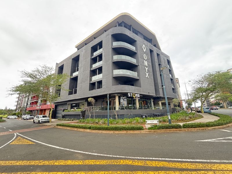 Modern multi-story apartment building featuring a dark grey facade, curved balconies with glass balustrades, and ground-floor commercial space.