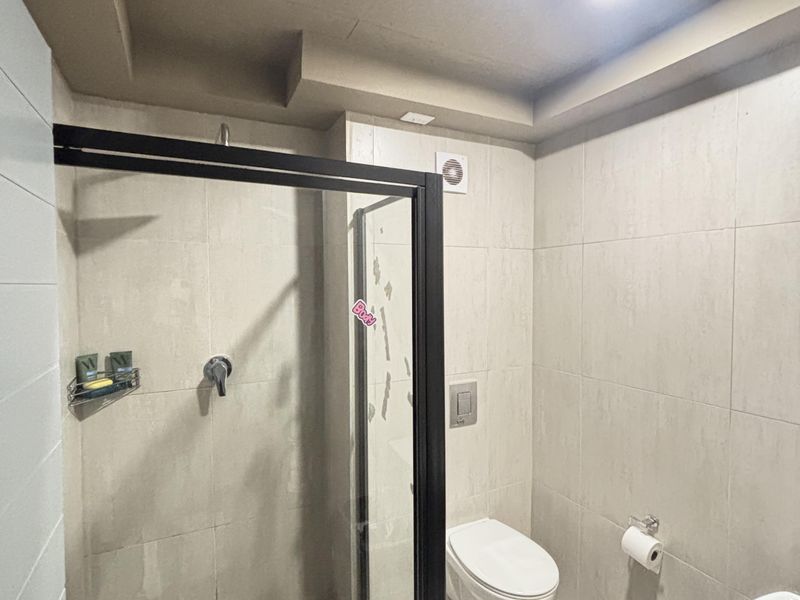 Modern bathroom featuring a walk-in shower with black-framed glass screen, wall-mounted toilet, and neutral floor-to-ceiling tiling.