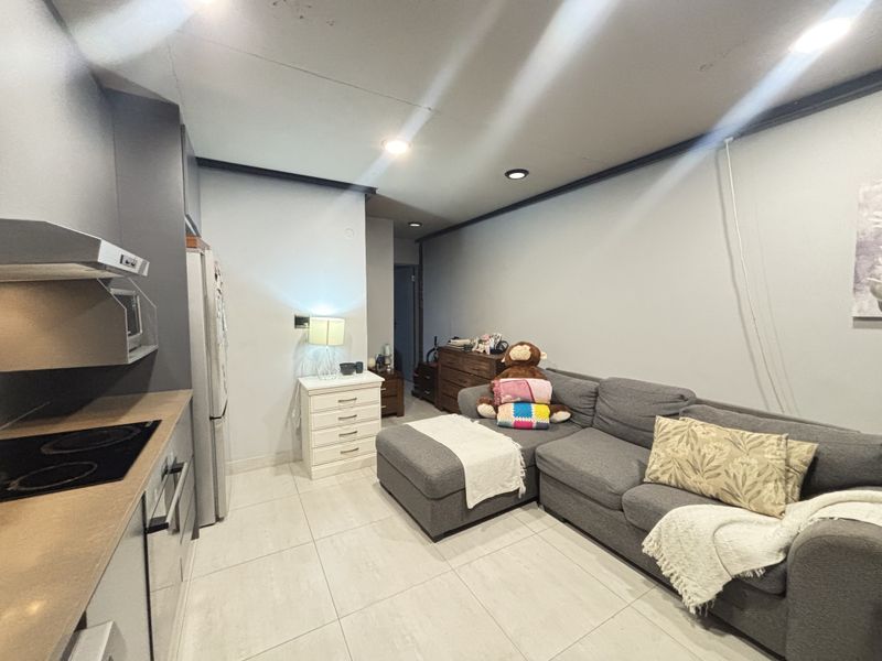 Open-plan living area featuring a compact kitchen with built-in cabinetry, electric cooktop, and tiled flooring throughout.
