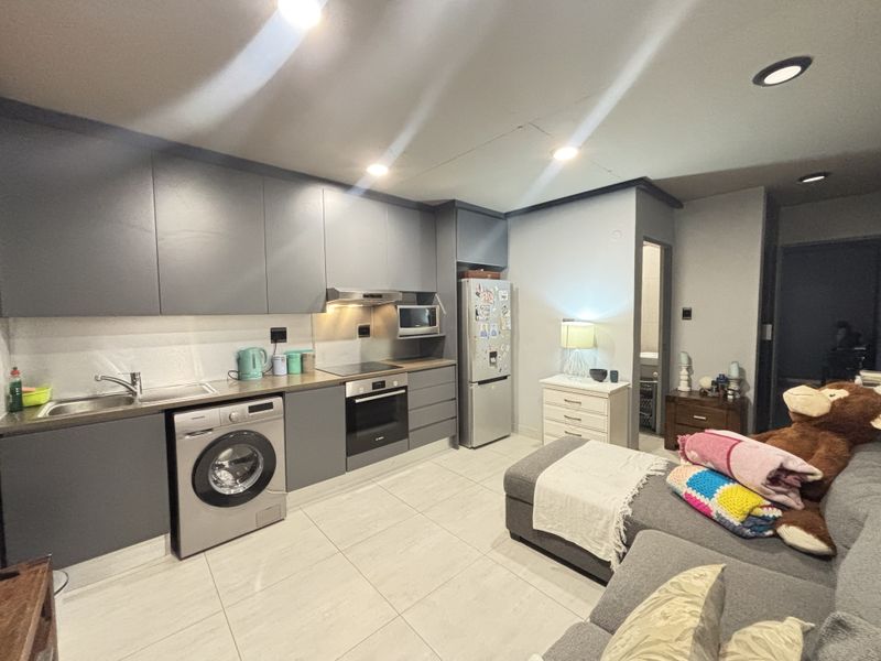Modern open-plan kitchen featuring sleek grey cabinetry, integrated appliances, and tiled flooring, seamlessly flowing into the living area.