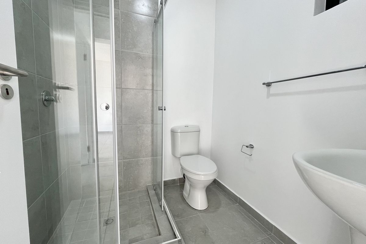A clean, modern bathroom featuring a glass-enclosed shower, pedestal basin, and toilet with neutral grey floor and wall tiling.