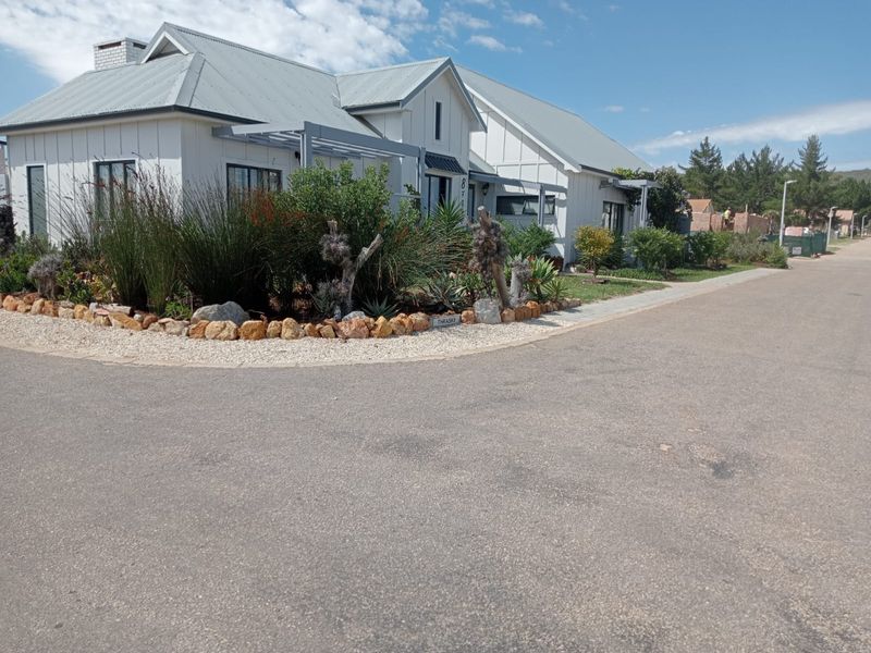 A well-maintained residential property featuring a modern farmhouse aesthetic with a metal roof, stone-edged landscaping, and a paved street-facing entrance.
