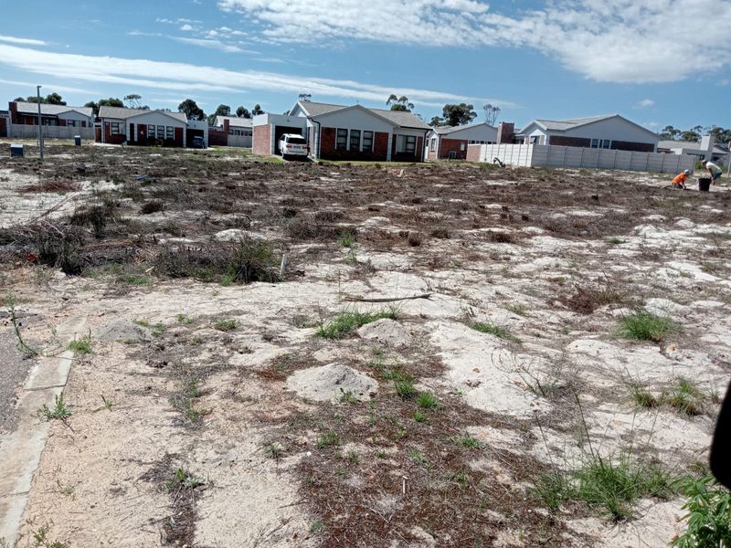 A vacant residential plot of land featuring sandy terrain, situated in a developed neighborhood with surrounding residential properties.
