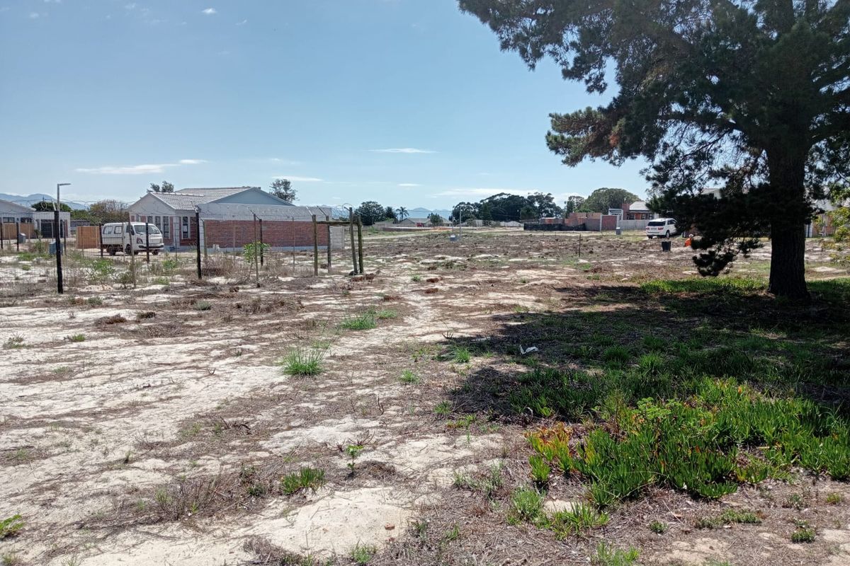 A vacant residential plot featuring sandy terrain, wire fencing, and a large mature tree, offering a clear space for future development.