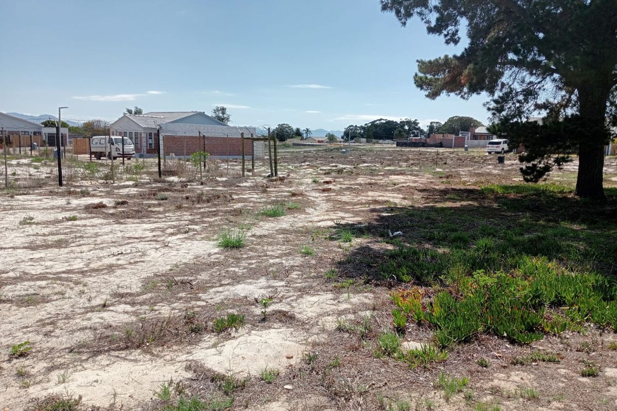 A vacant residential plot featuring sandy terrain, wire fencing, and a large mature tree, offering a clear space for future development.