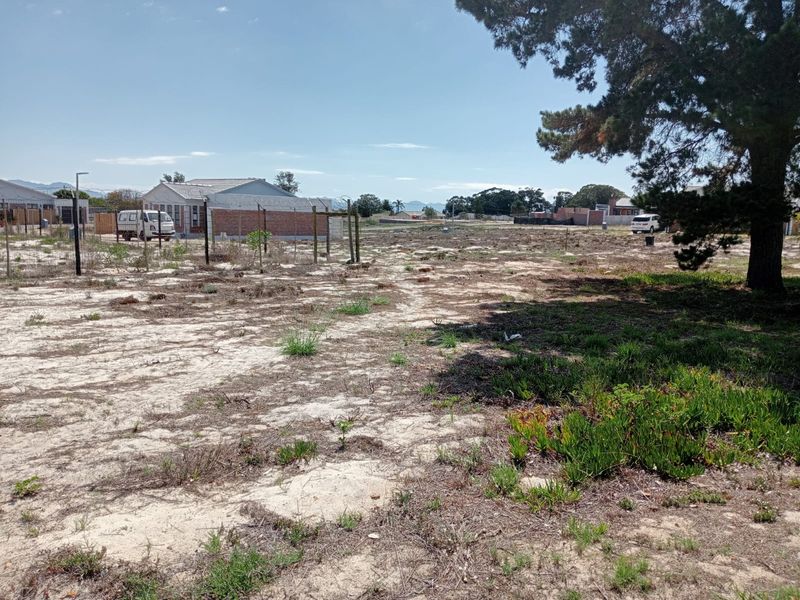A vacant residential plot featuring sandy terrain, wire fencing, and a large mature tree, offering a clear space for future development.