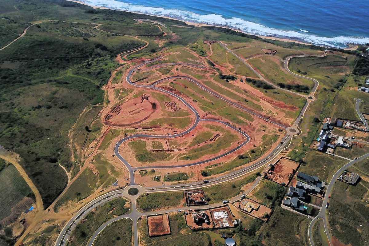 Aerial view of a residential development site featuring paved roads, roundabouts, and coastal proximity.