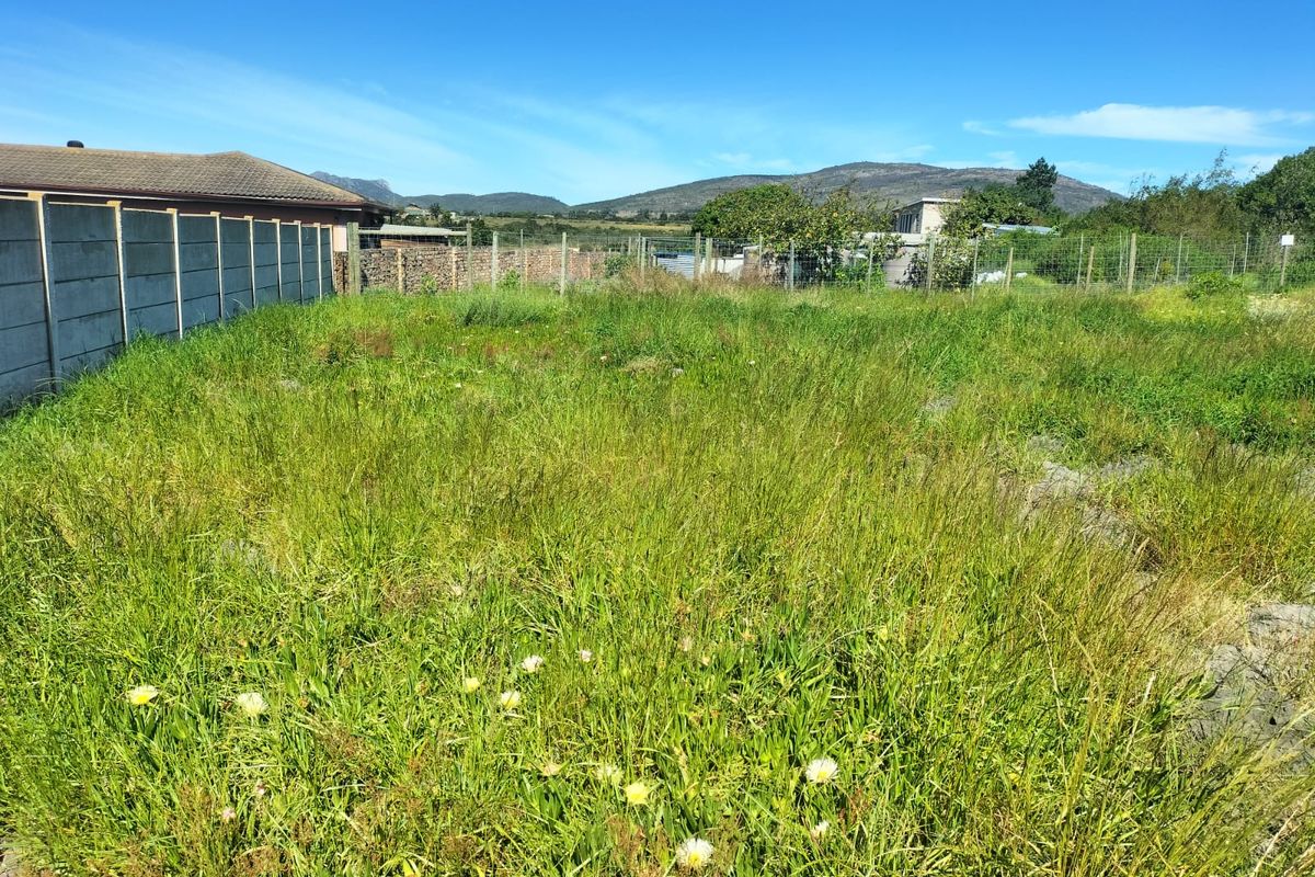 A vacant residential plot featuring overgrown grass, enclosed by a combination of precast concrete boundary walls and wire mesh fencing.