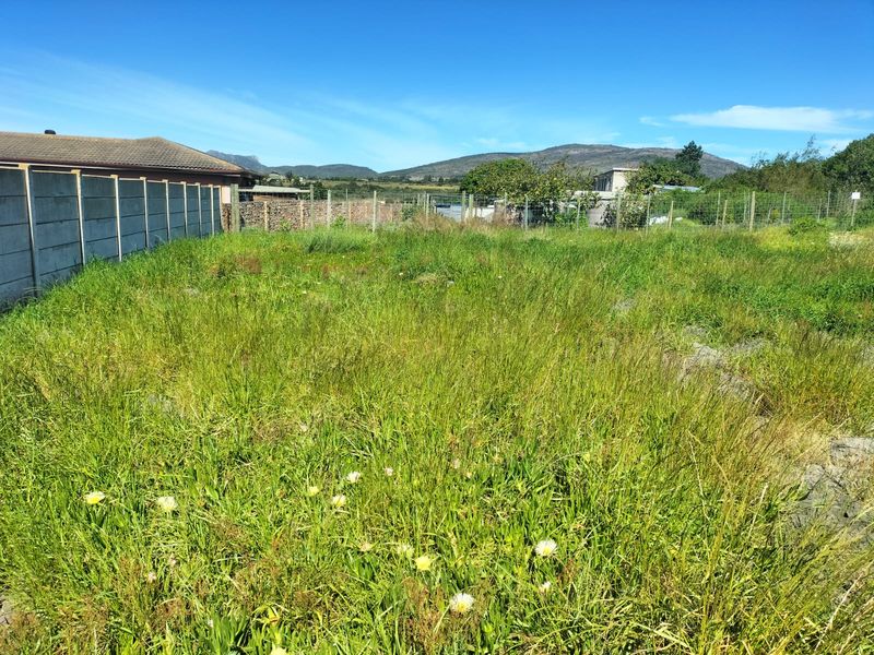 A vacant residential plot featuring overgrown grass, enclosed by a combination of precast concrete boundary walls and wire mesh fencing.