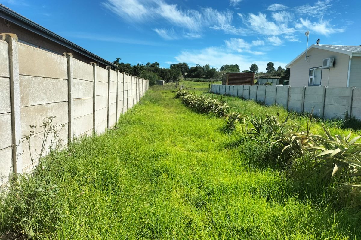 A vacant residential plot featuring a grass lawn enclosed by precast concrete boundary walls on both sides.