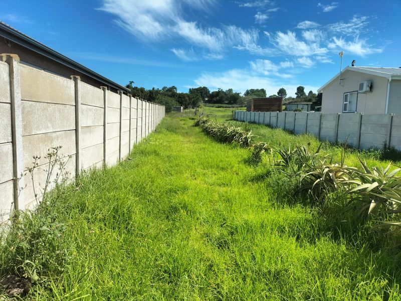 A vacant residential plot featuring a grass lawn enclosed by precast concrete boundary walls on both sides.